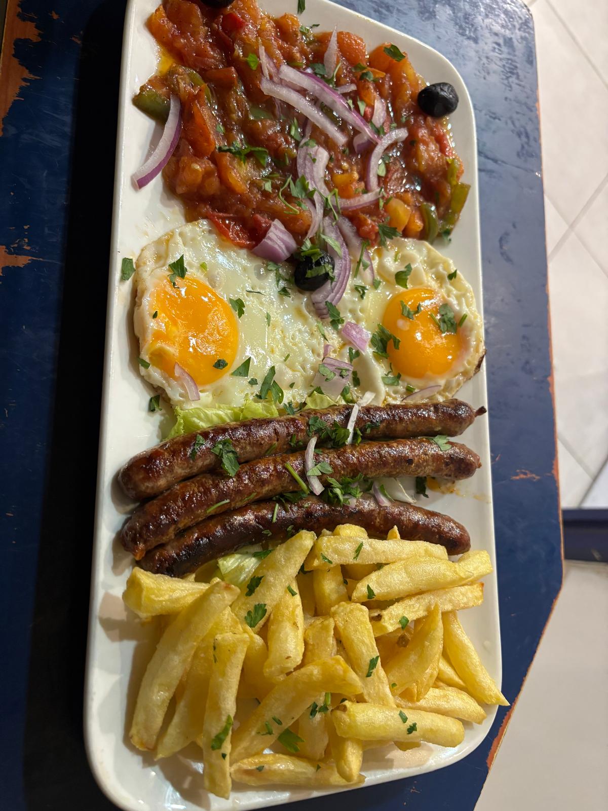 Mokli merguez ou escalope : Le mokli — sauce tomate fraîche, poivron vert frit, œuf au plat, frites maison —, avec merguez ou escalope